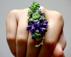 a woman's hand holding a ring with purple and green flowers on the middle