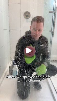 a man sitting on the floor in front of a shower holding a glove with water coming out of it