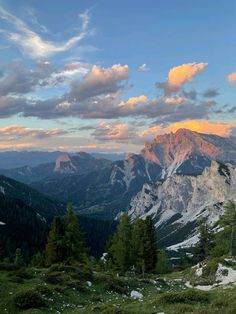 the mountains are covered in snow and trees as the sun is setting over them,