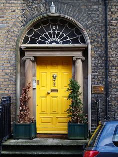 a yellow door is in the middle of a brick building with potted plants on either side