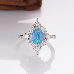 Mesmerizing Fire in Sterling Silver: Mia Ring. This handcrafted ring features a captivating natural blue fire opal, its brilliance flickering with every move. A timeless treasure that adds a touch of magic to any outfit (sizes 3.5-14.25). ✦ DETAILS ✦ ✧ Handcrafted  ✧ Fire opal and natural crystals  ✧ Sizes 3.75-14.25 ✧ This ring  will arrive ready to gift in a Kherish Jewelry Pouch. ✧ Due to the nature of the handmade process, each piece may slightly vary in color, size, shape, and contain natur Opal Halo Ring As Gift, Opal Halo Rings As Gifts, Opal Halo Ring For Gift, Opal Halo Jewelry As Gift, Opal Halo Rings For Gifts, Opal Promise Ring With Center Stone, Opal Ring With Center Stone As Gift, Opal Ring With Center Stone For Gift, Opal Jewelry With Halo Setting For Gift