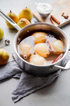 a pot filled with liquid next to pears and cinnamon on top of a table