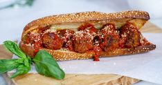 a meatball sub sandwich with tomato sauce and basil on a cutting board next to it