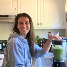 a woman holding a blender full of green smoothie in her hand and smiling at the camera