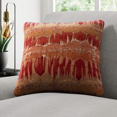 an orange and red pillow sitting on top of a gray couch next to a potted plant