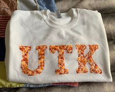 a white t - shirt with the word utk spelled out in orange sprinkles