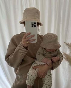 a woman is holding a baby and taking a selfie with her cell phone while wearing a hat