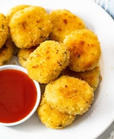 some fried food on a plate with ketchup and dipping sauce in the bowl