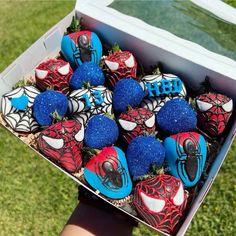 a box filled with cupcakes covered in blue and red frosted spiderman decorations