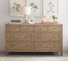 a dresser with two pictures on the wall and flowers in vases next to it