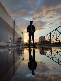 a man in a suit and tie standing next to a body of water at sunset