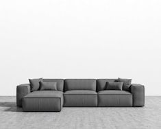 a gray couch sitting on top of a floor next to a white wall with pillows