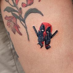 a deadpool tattoo on the side of a woman's thigh, with flowers behind it