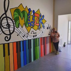 a woman standing next to a colorful wall with musical notes painted on it and rainbow colors