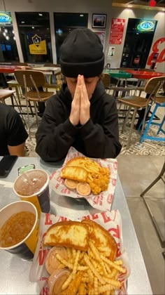 a person sitting at a table with food in front of him and his hands covering their face