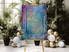 an easel with a painting on it in front of balloons and plants, along with other decorations