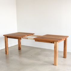 two wooden tables sitting next to each other on top of a cement floor in front of a white wall