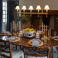 a dining room table is set with plates and bowls, candles, and fruit on it