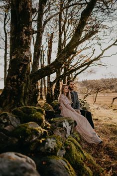 a man and woman sitting next to each other in front of trees with moss growing on them