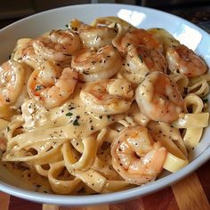 a white bowl filled with pasta and shrimp on top of a wooden table next to a knife