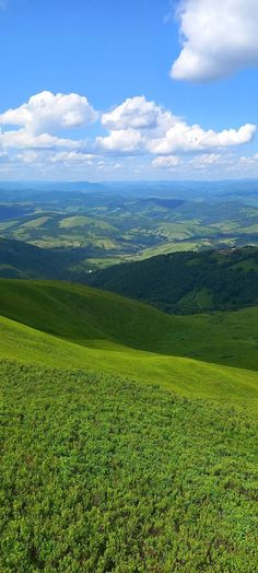 a grassy hill with rolling hills in the distance and blue skies above it on a sunny day