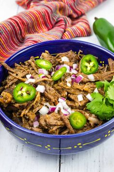 a blue bowl filled with shredded beef and green peppers on top of a white table