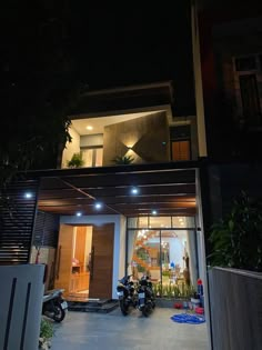 two motorcycles are parked in front of a house at night with lights on the windows