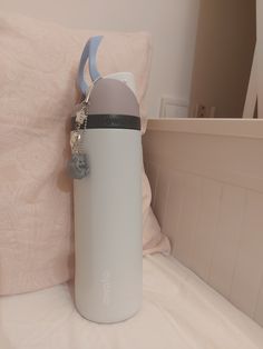 a white and gray bottle sitting on top of a bed next to a pink pillow