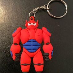 a red and blue robot keychain sitting on top of a black table next to a pair of scissors