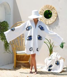 "Stay trendy and comfortable with the Evil Eye Kaftan Kimono. Made from 100% organic cotton and hand-printed with the timeless evil eye design, this Greek goddess-style kaftan is the perfect cover-up for all your summer needs.  Whether you're spending the day at the beach, picnicking in the park, or just lounging at home, the lightweight, breathable fabric will keep you cool and comfortable, and protect you from evil spirits and evil eyes. This eco-friendly and quick-drying kimono is an excellent choice for summer activities. Features *100% Cotton  *Soft, Light & Fluffy *An adjustable waist belt secures the robe from the front. Size: Length: 35.5\" - 90cm     Width: 33.5\" - 85 cm Model Height :5′ 6\"- 168 cm Care *Machine wash cold at a gentle cycle. *No bleach. *Iron on the reverse side White V-neck Kimono For Festival, White V-neck Summer Kimono, White V-neck Kimono For Vacation, White Open Front Kimono For Festival, White Embroidered Open Front Kimono, White Long Sleeve Cardigan For Beach Cover-up, White Tunic Kimono For Beach Cover-up, White Tunic Kimono For Vacation, Traditional White Kimono For The Beach