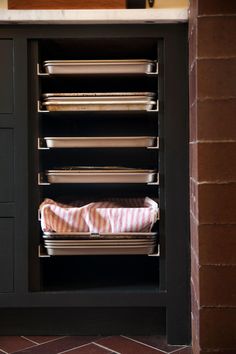 an open cabinet with dishes in it on top of a tile floor and red brick wall