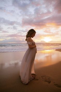 a pregnant woman standing on the beach at sunset