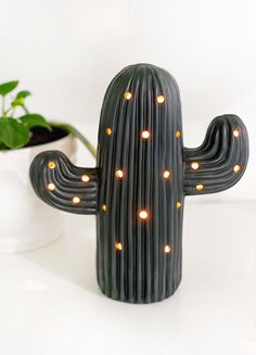 a ceramic cactus with lights on it sitting next to a potted plant and white wall