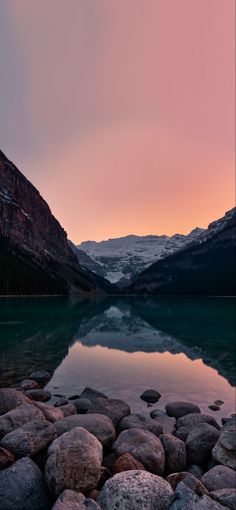 a lake surrounded by mountains with rocks in the foreground and water on the other side