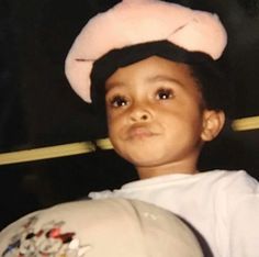 a young boy wearing a white hat and holding a stuffed animal in his arms, looking at the camera