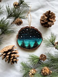 a christmas ornament hanging from a tree with pine cones and fir trees in the background