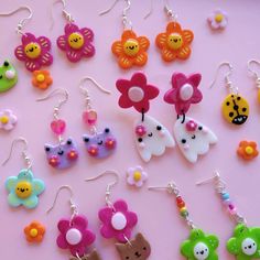 many different colored earrings on a pink surface with flowers and butterflies attached to the ear wires