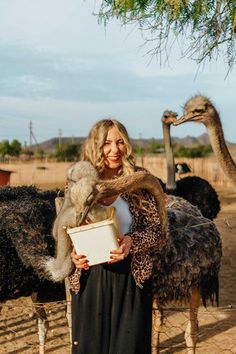 a woman standing in front of an ostrich and holding a piece of paper