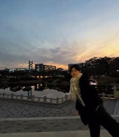 a woman is standing in front of a lake at dusk with her cell phone up to her ear