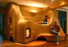 two men sitting on a bench in front of a fake mushroom like house with a fireplace