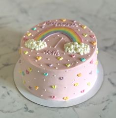 there is a pink cake with rainbows and clouds on it