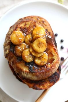 pancakes with bananas and blueberries are on a white plate next to a silver fork