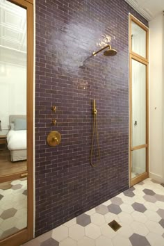 a bathroom with a brick wall and gold fixtures on the shower head, hand held by a brass faucet