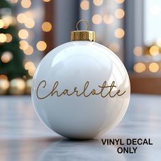 a white ornament with the word charlotte written on it and a christmas tree in the background