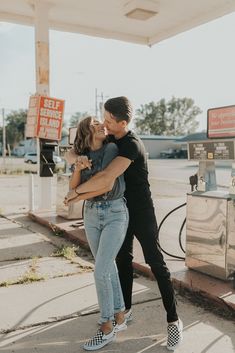 a man and woman kissing in front of a gas station