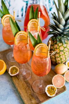 three glasses filled with orange juice and garnished with green leaves on a cutting board