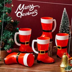 red and white christmas mugs with santa's hat on them next to a tree