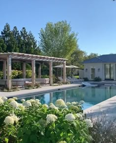 an outdoor swimming pool surrounded by greenery and shrubs with white flowers in the foreground