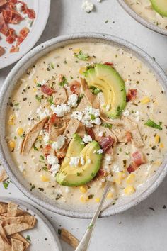 two bowls filled with soup and topped with cheese, bacon, avocado and other toppings