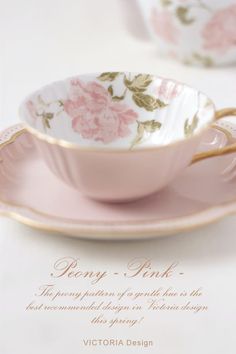 a pink tea cup and saucer sitting on top of a white table with gold trim